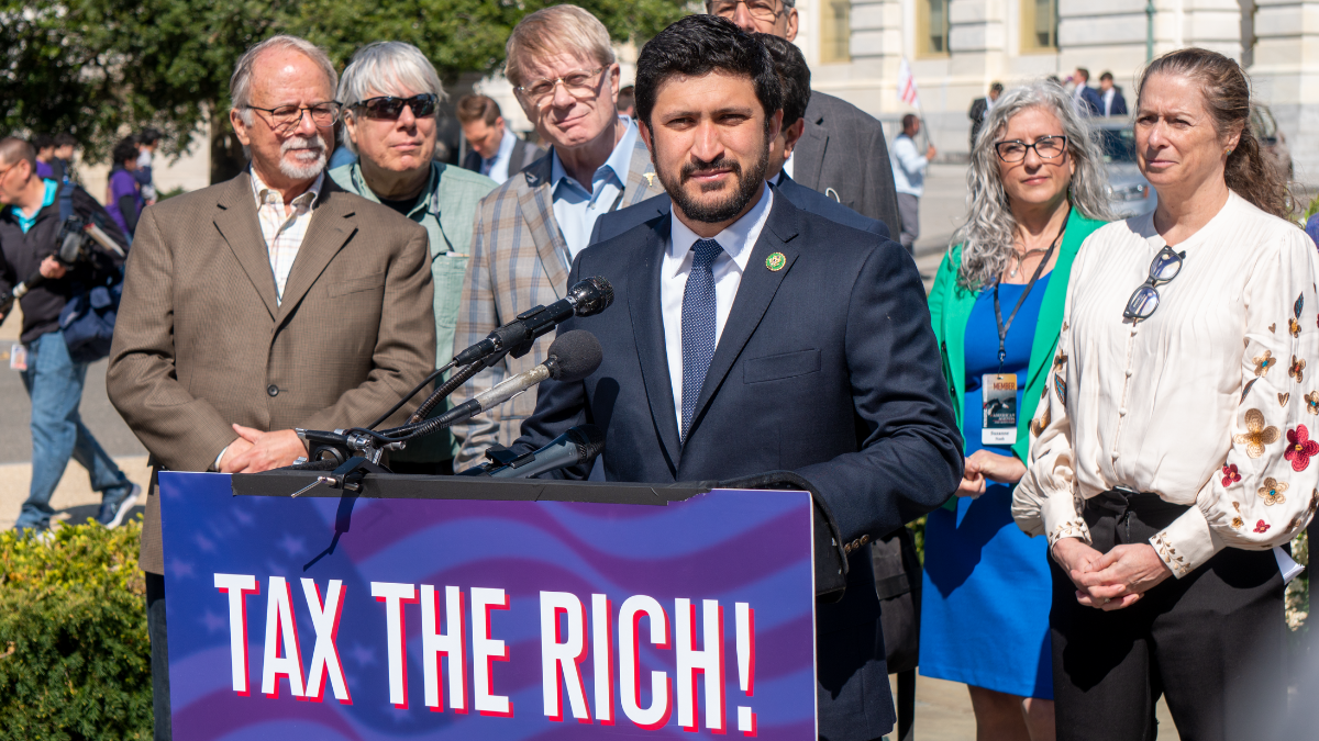 Congressman Casar at a press conference with a podium reading "Tax the Rich!"