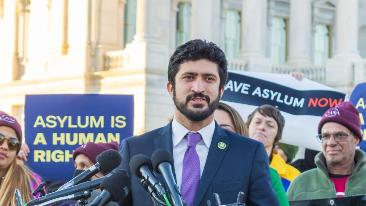 Congressman Greg Casar standing in front of a podium with microphones with immigration activists behind him