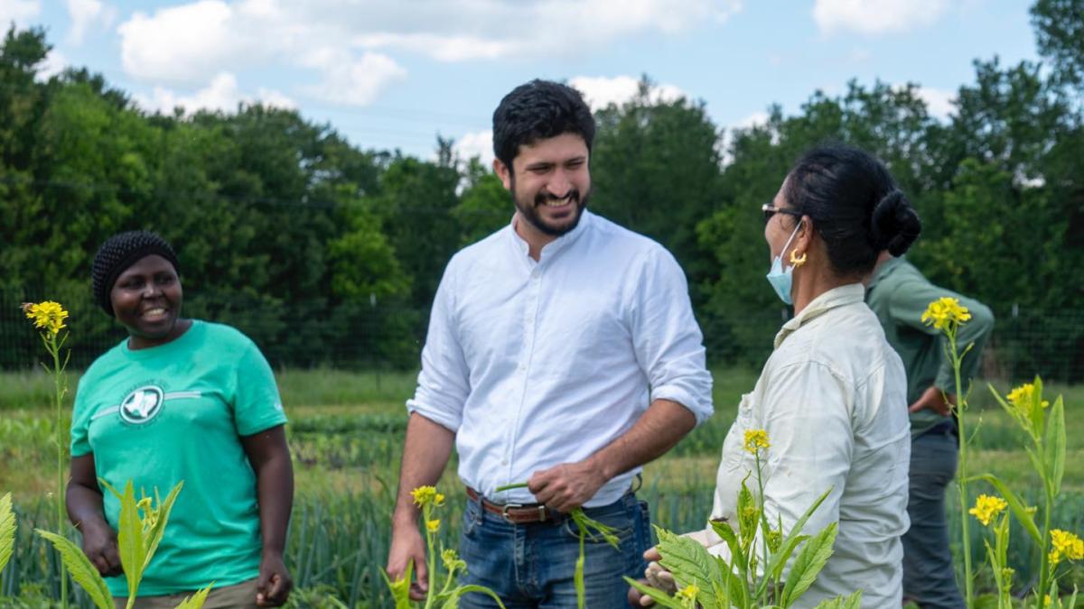 Congressman Greg Casar talking with two constituents in a farm field 