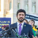 Congressman Greg Casar standing in front of a podium with microphones with immigration activists behind him